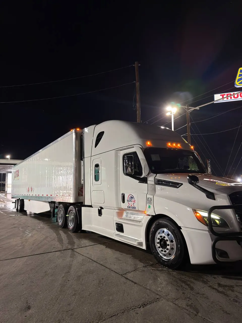A white SDS UZ semi-truck and trailer at a truck stop at night