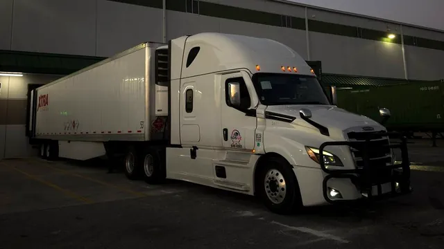 A white SDS UZ semi-truck with its trailer at a warehouse loading dock at dusk